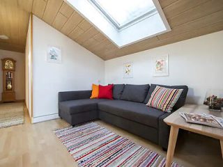 Cozy attic living room with a comfortable grey sofa, vibrant cushions, and a striped rug, featuring a sloped ceiling with a skylight